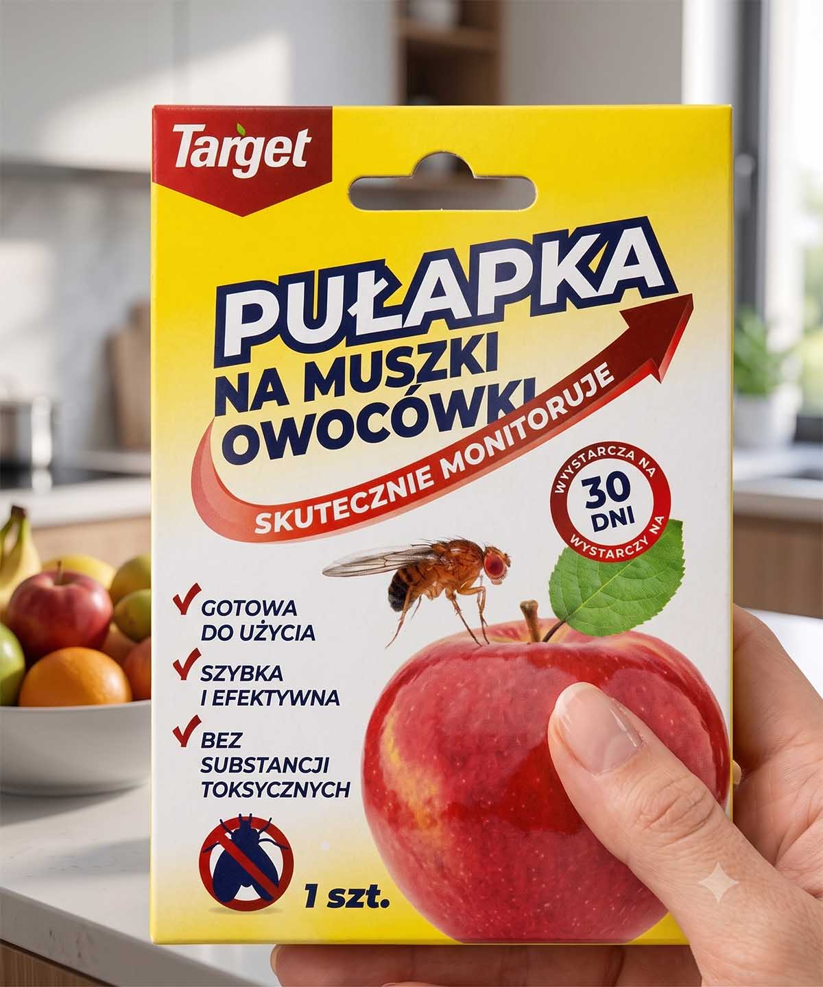 Opakowanie pułapki na muszki owocówki Target Kobieca dłoń trzymająca oryginalne, żółto-białe opakowanie blister pułapki na muszki owocówki Target z grafiką czerwonego jabłka.
