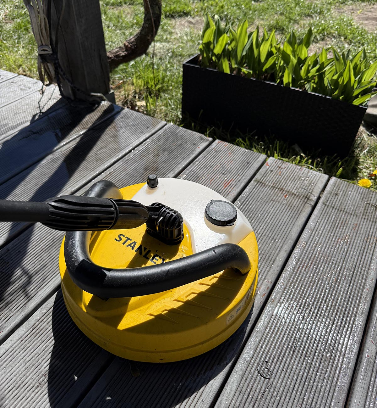 Przystawka Patio Cleaner Deluxe myjki Stanley Fatmax na deskach tarasowych z widocznym zbiornikiem na detergent.