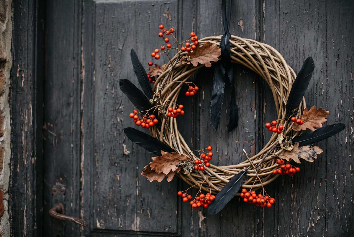 Wianek halloweenowy z jarzębiny i czarnych piór na drzwiach Wianek na drzwi z wikliny z gałązkami jarzębiny, czerwonymi owocami, suszonymi liśćmi dębu i czarnymi piórami